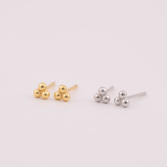 Photo featuring silver and gold ball stud earrings arranged in a triangular formation with three small ball shapes fused together. Captured from a 45-degree angle to showcase the entirety of the earrings' design, offering a blend of elegance and uniqueness.