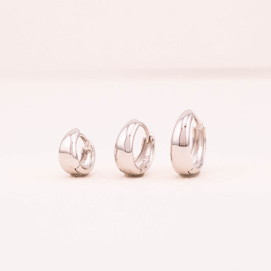 Three silver tapered hoop earrings, varying in size, arranged side by side. A chunky hoop showcasing the difference in sizes. The photo is taken from the front view, highlighting the unique design and varying thickness of each earring.