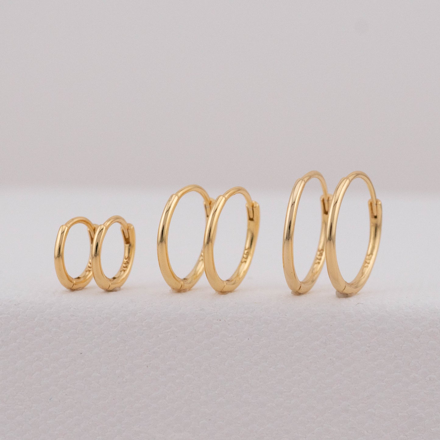 Gold mini huggie hoop earring sets in three different sizes are displayed at an angled view