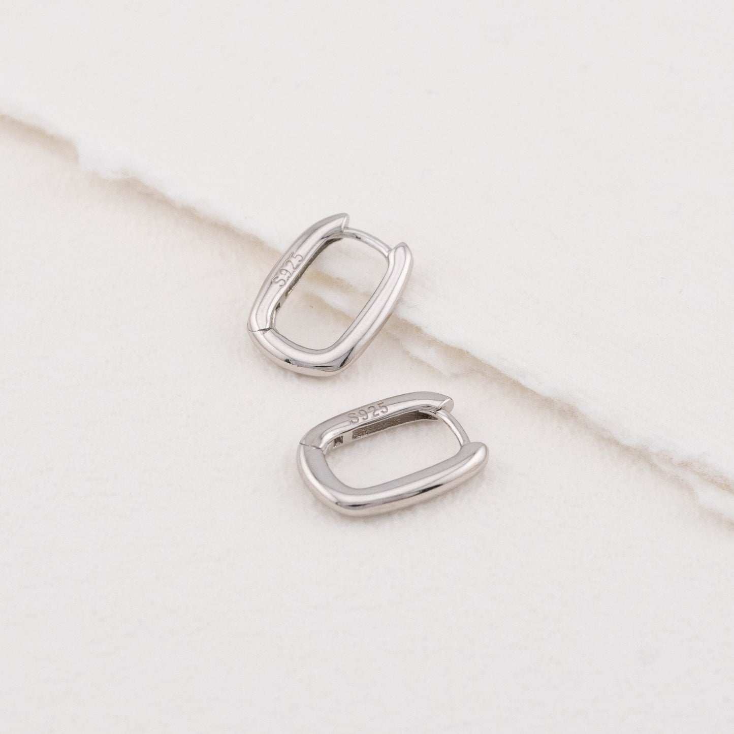 Mini sterling silver rectangular hoop earrings: one angled, one flat, both stamped "S925".