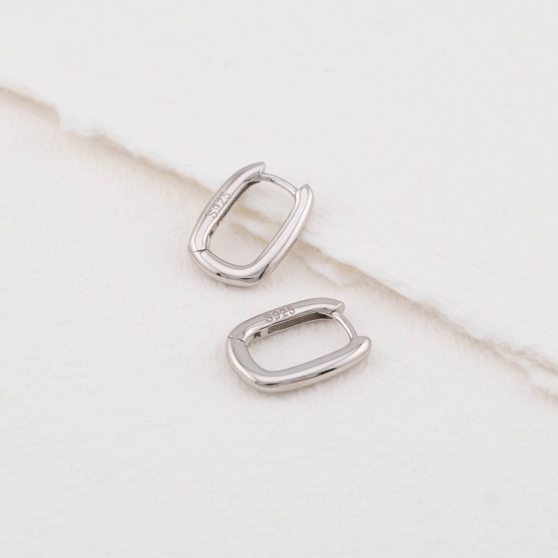 Mini sterling silver rectangular hoop earrings: one angled, one flat, both stamped "S925".