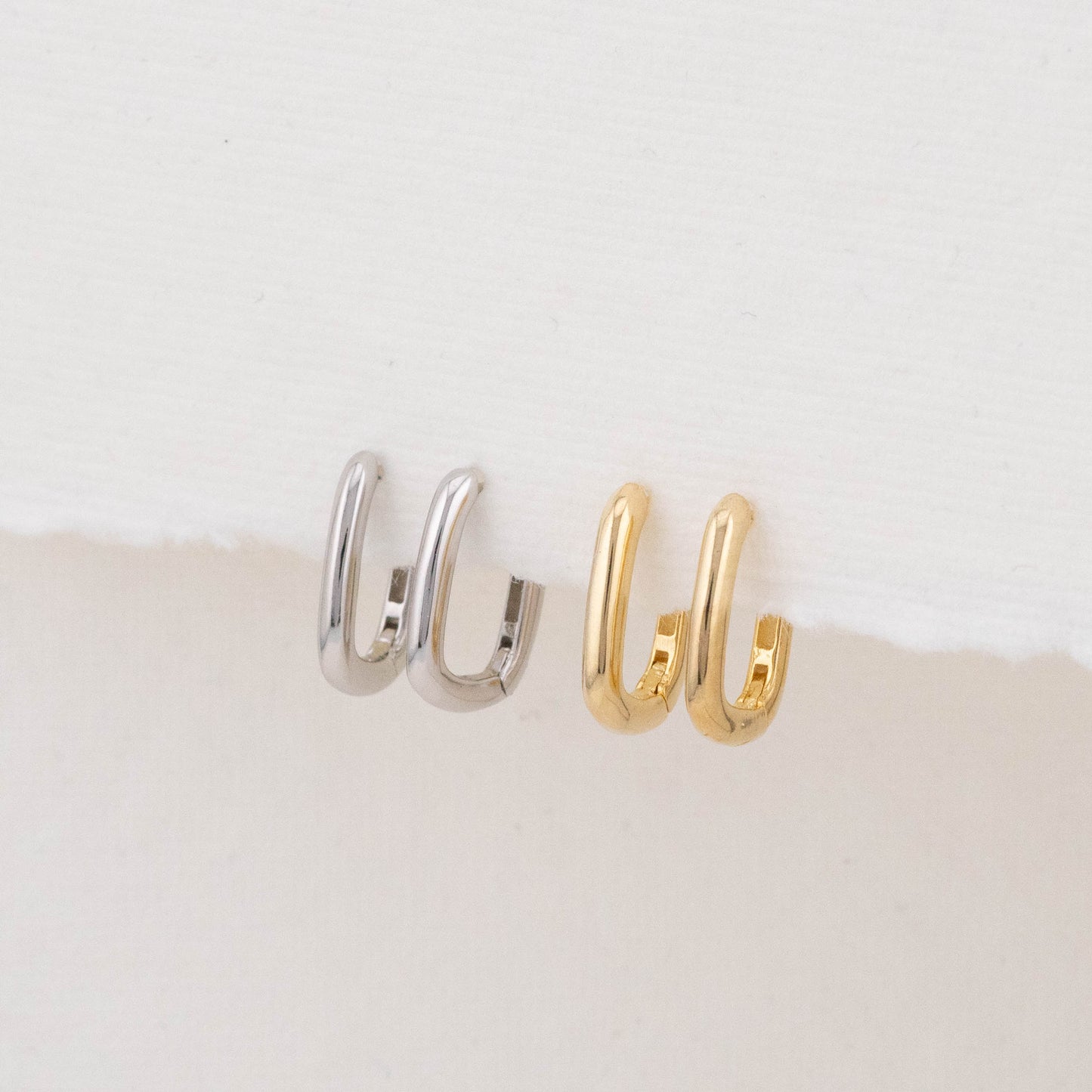 Two mini rectangular hoop earrings (one gold, one silver) are displayed side by side on a holder