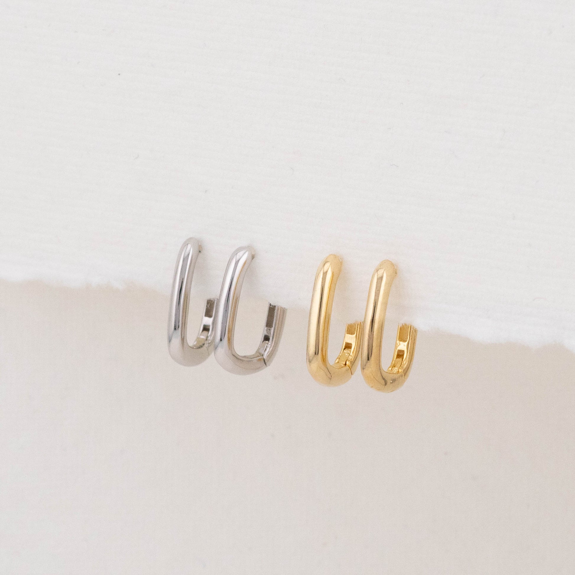 Two mini rectangular hoop earrings (one gold, one silver) are displayed side by side on a holder