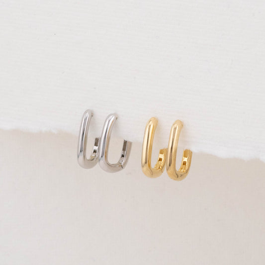 Two mini rectangular hoop earrings (one gold, one silver) are displayed side by side on a holder