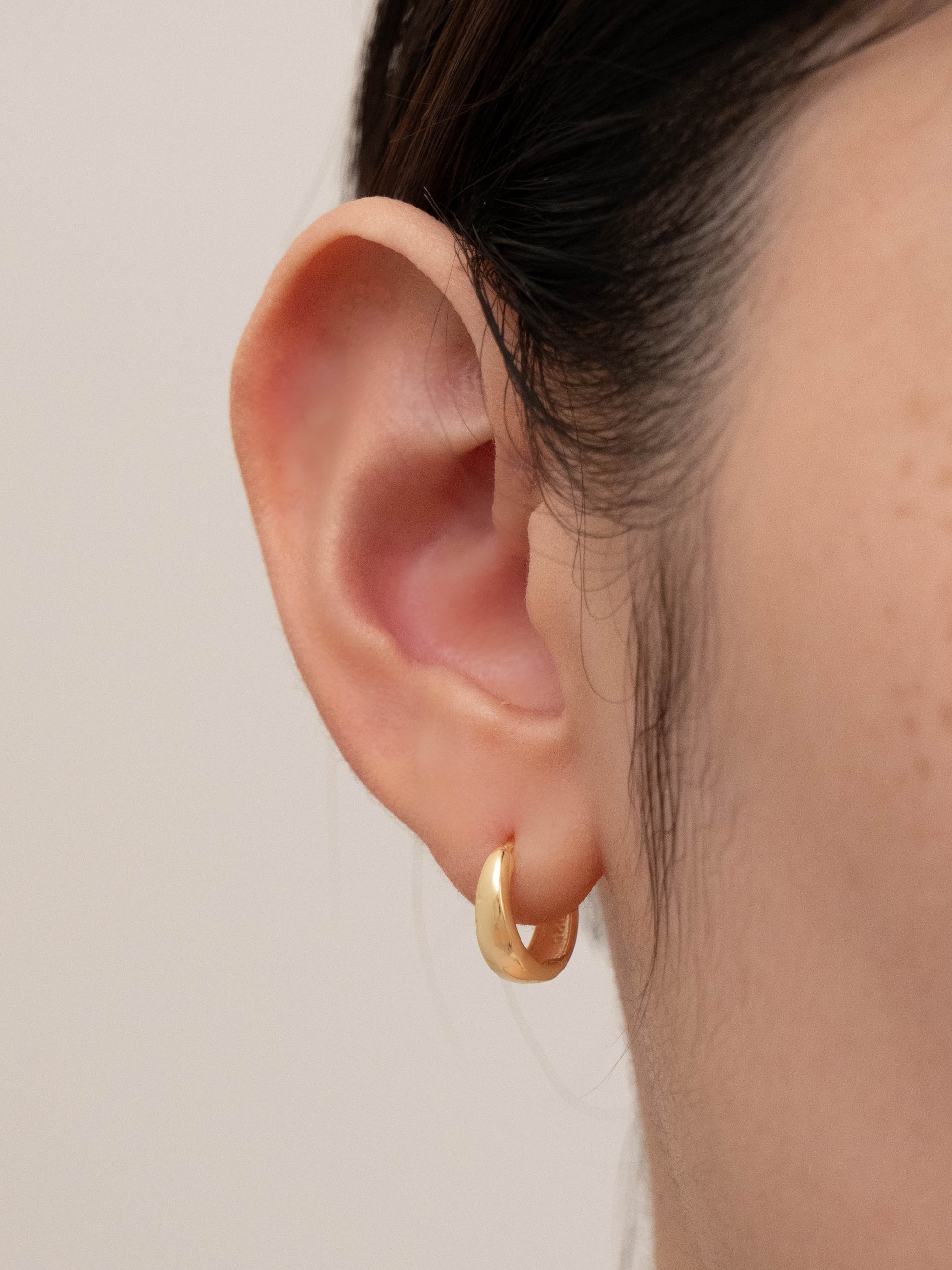 Huggies gold earring shown worn in one ear, illustrating its look in a single hole.