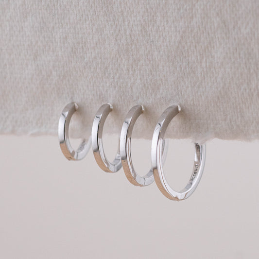 A set of silver stacking earrings on a stand, displaying different sizes for multiple piercings.