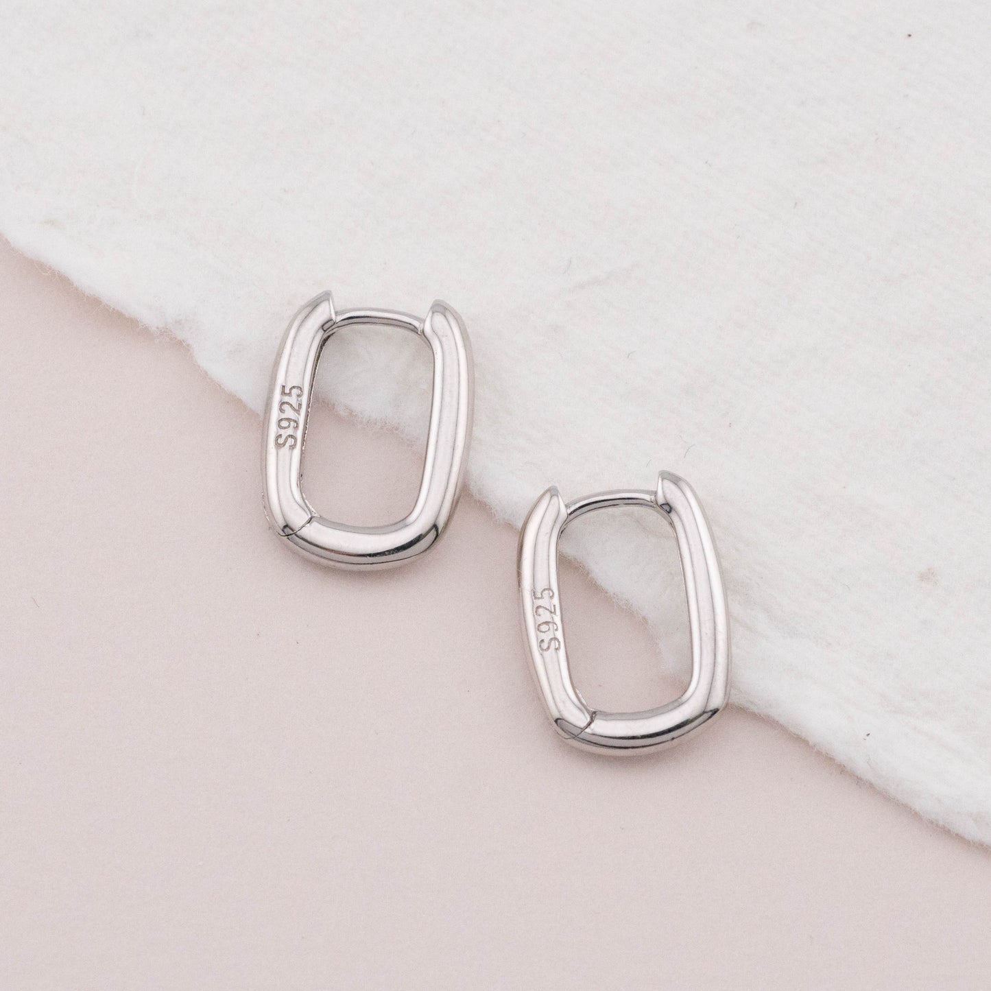 Mini chunky sterling silver rectangular hoops on white surface, top view showing bold thickness.