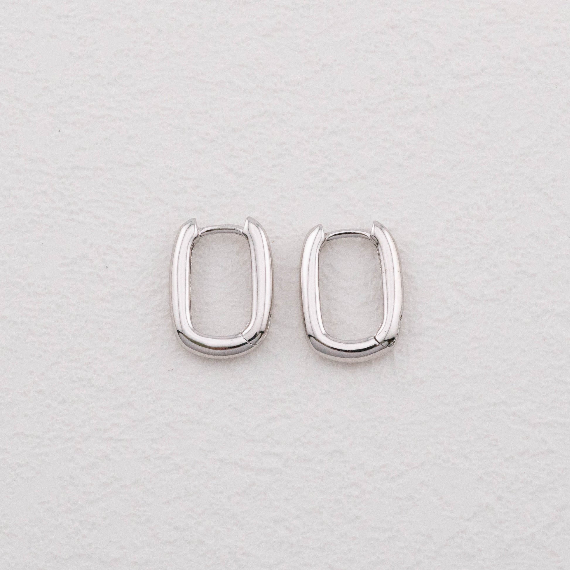 Mini chunky sterling silver rectangular hoop earrings on white surface, top view showing bold shape.