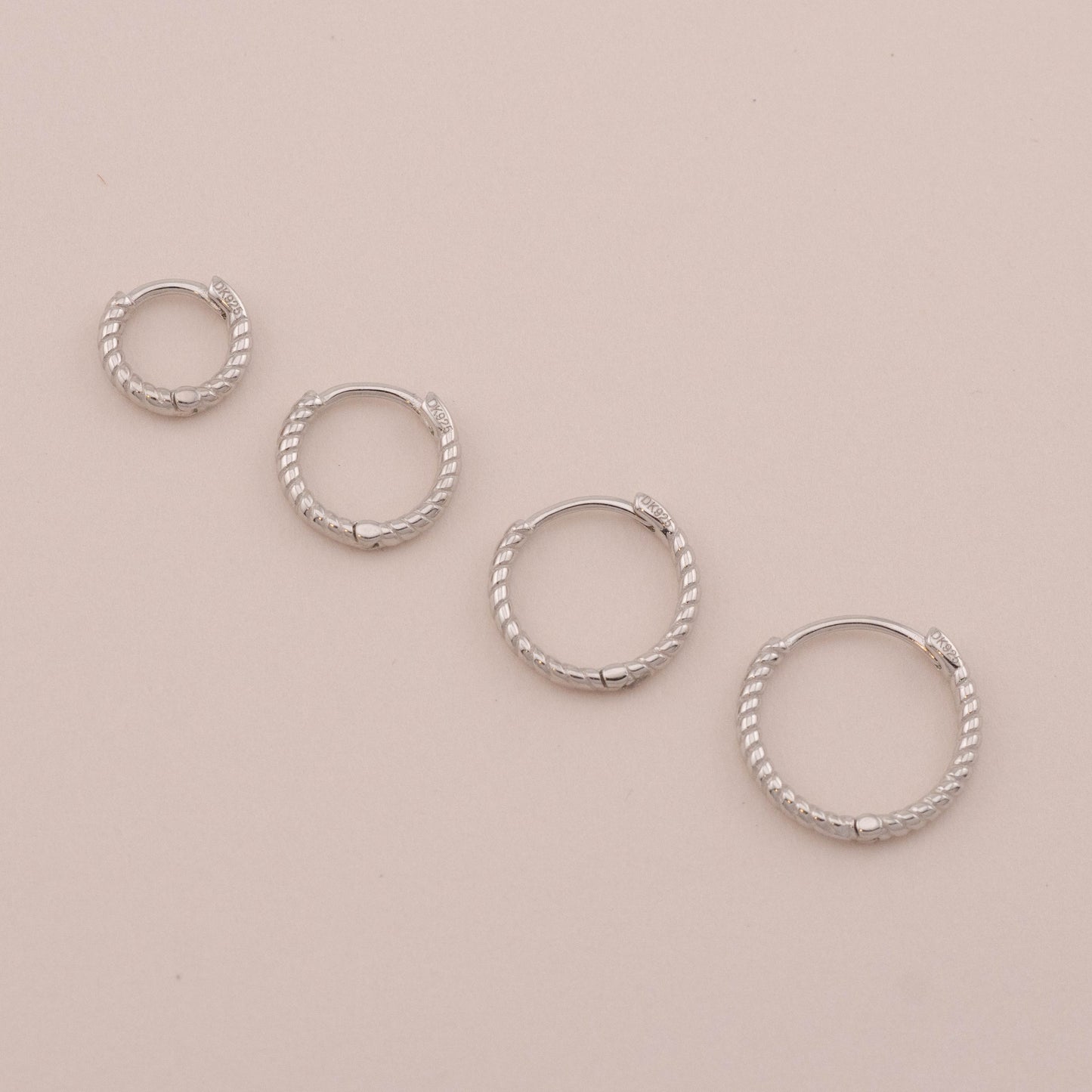 4 sizes of small huggie hoops laid down, showing hinged closures for everyday wear.