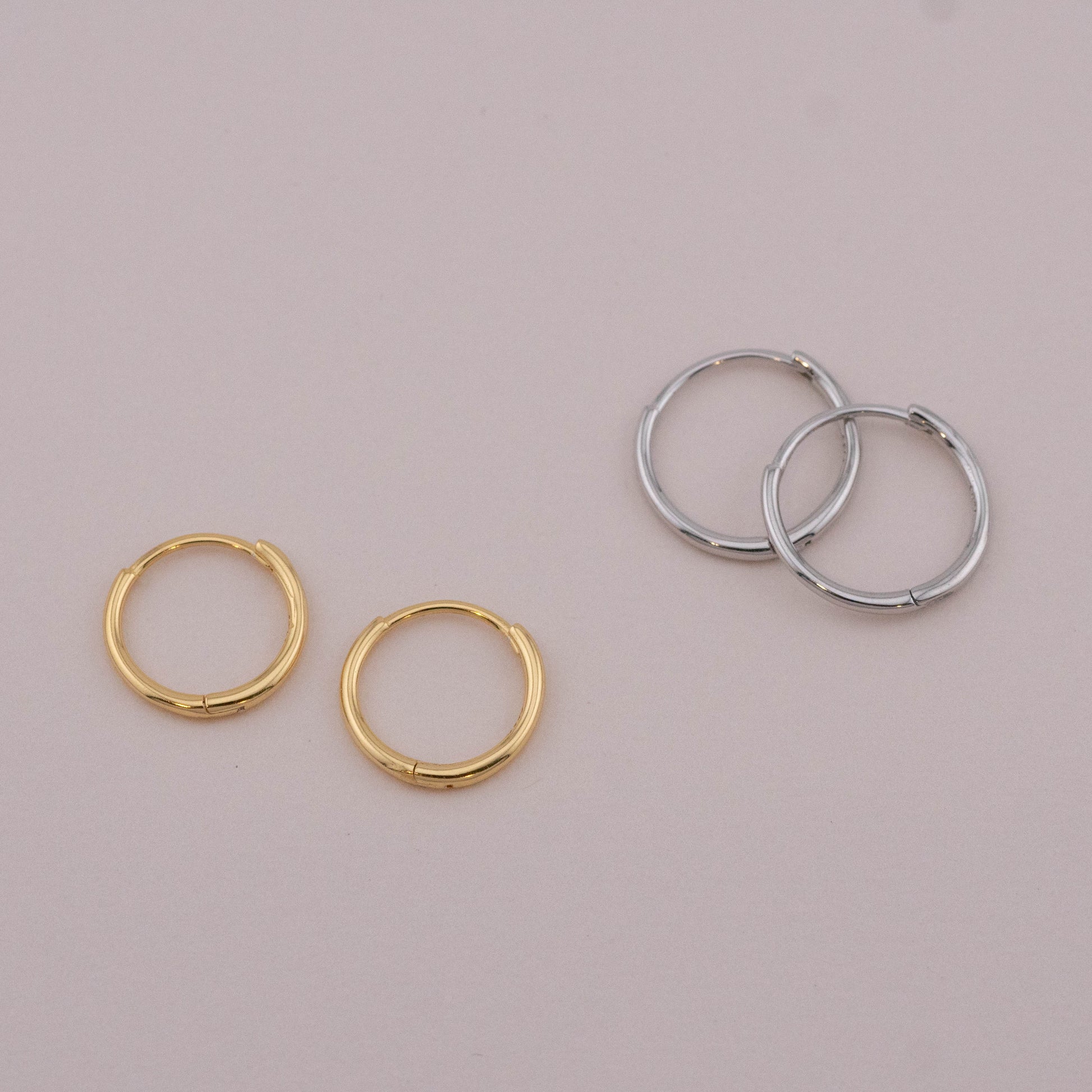 Gold and silver huggie hoops with hinged closures, shown on a surface, ideal for multiple piercings.